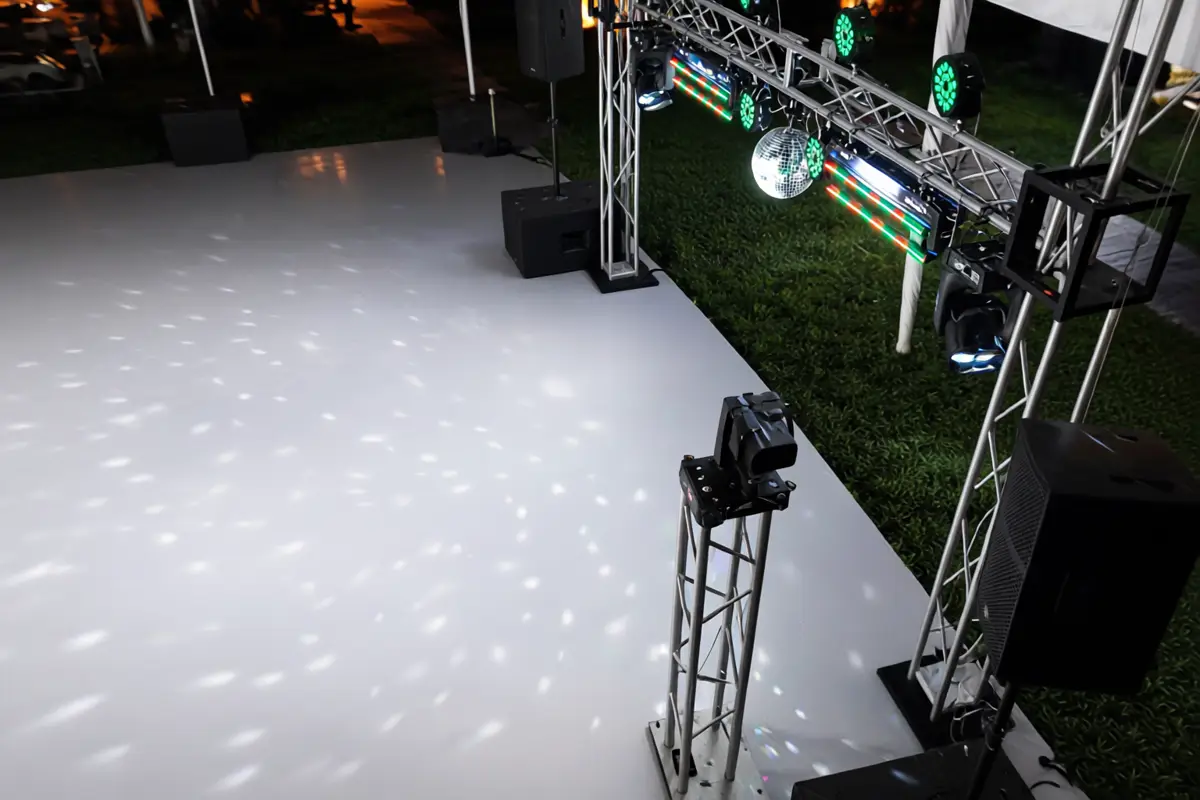 Estructura de truss con cabezas móviles iluminando una pista blanca en jardín de noche